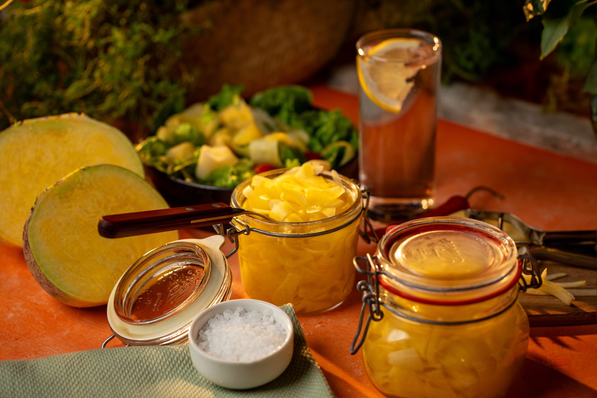 Jars of pickled yellow root vegetables, fresh slices, salt, and a green salad.