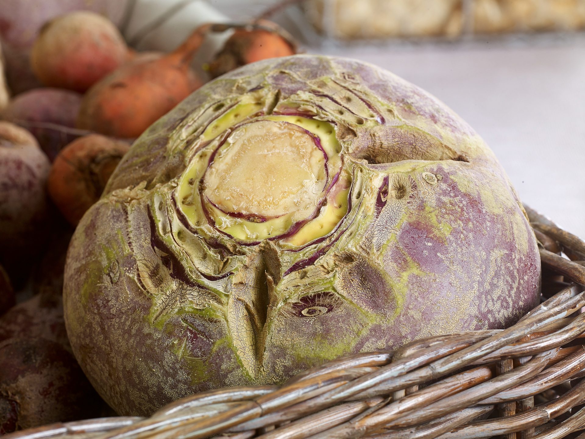A large, purplish-green rutabaga with a visible yellow core, nestled in a rustic woven basket.