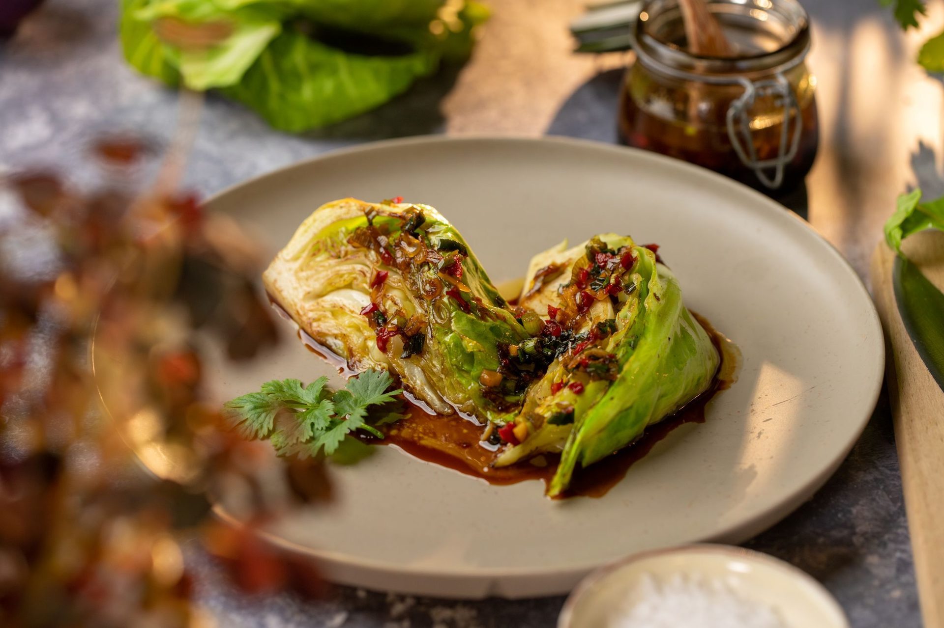 Seared cabbage with savory sauce, chili, and fresh cilantro garnish on a beige plate, with a jar of sauce.