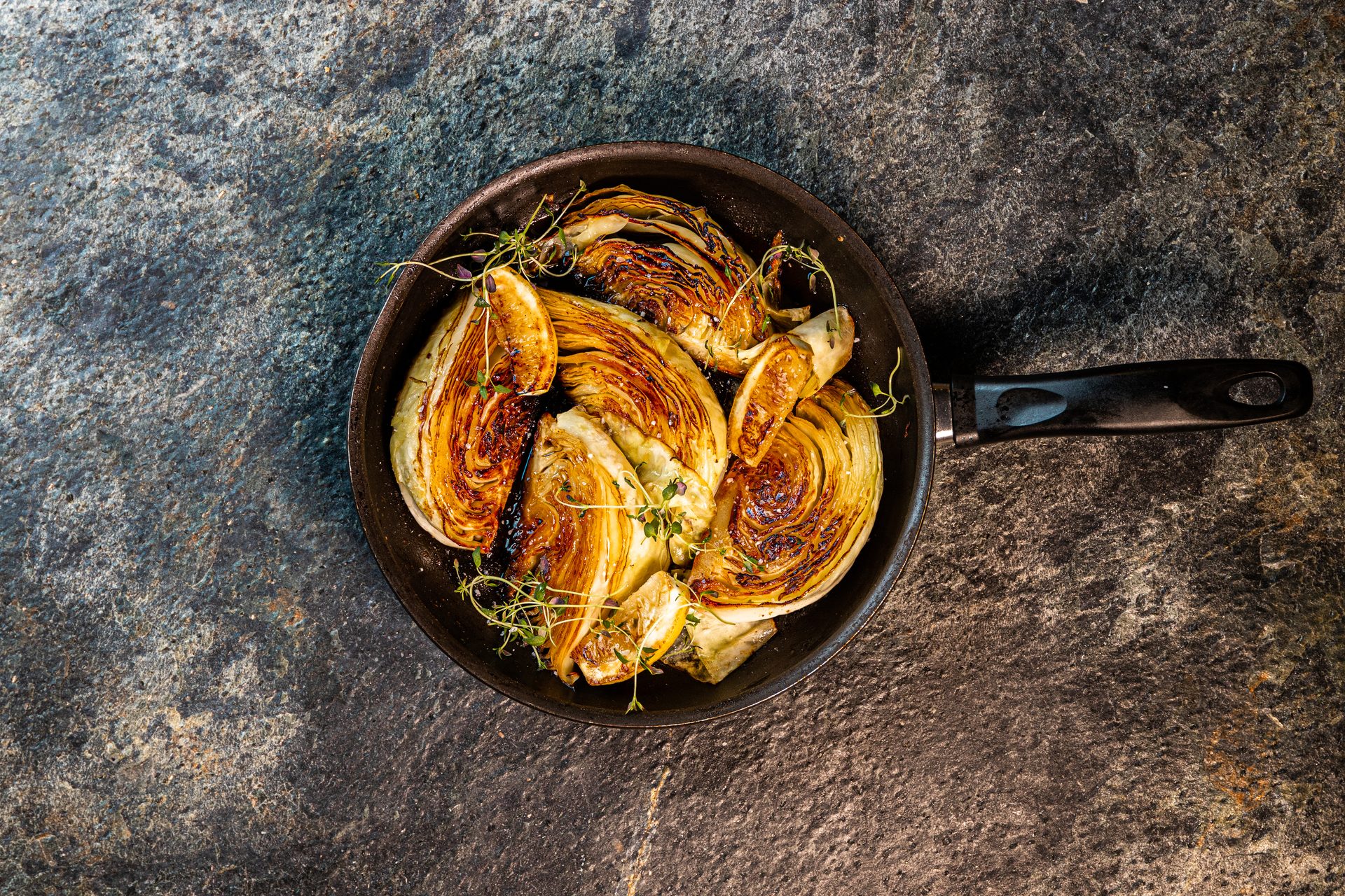 Pan-roasted fennel with herbs in a black skillet on a dark, textured background.