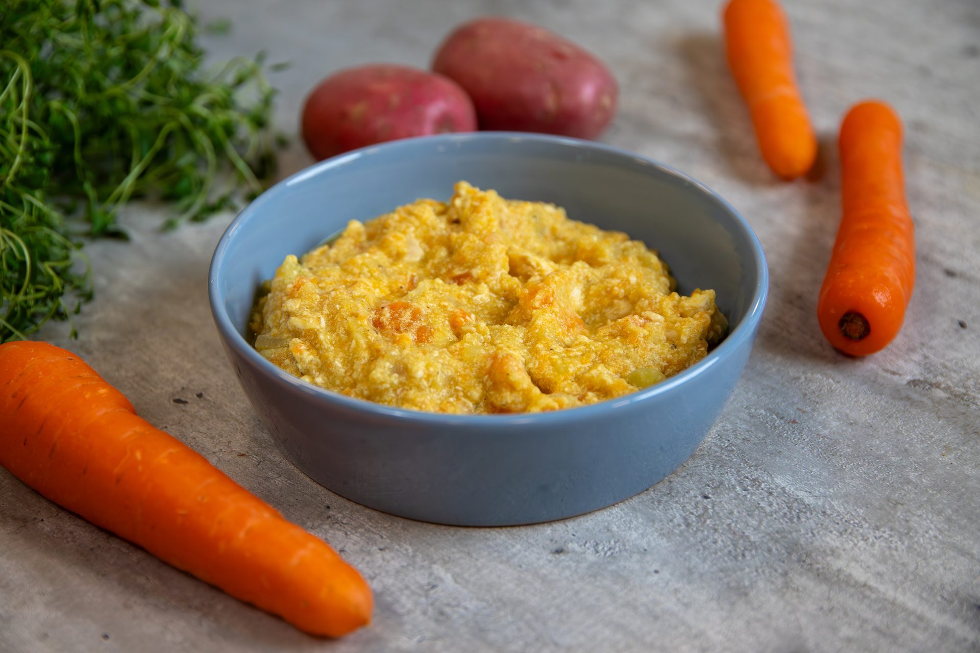 A blue bowl of mashed root vegetables, including carrots and potatoes, with herbs.