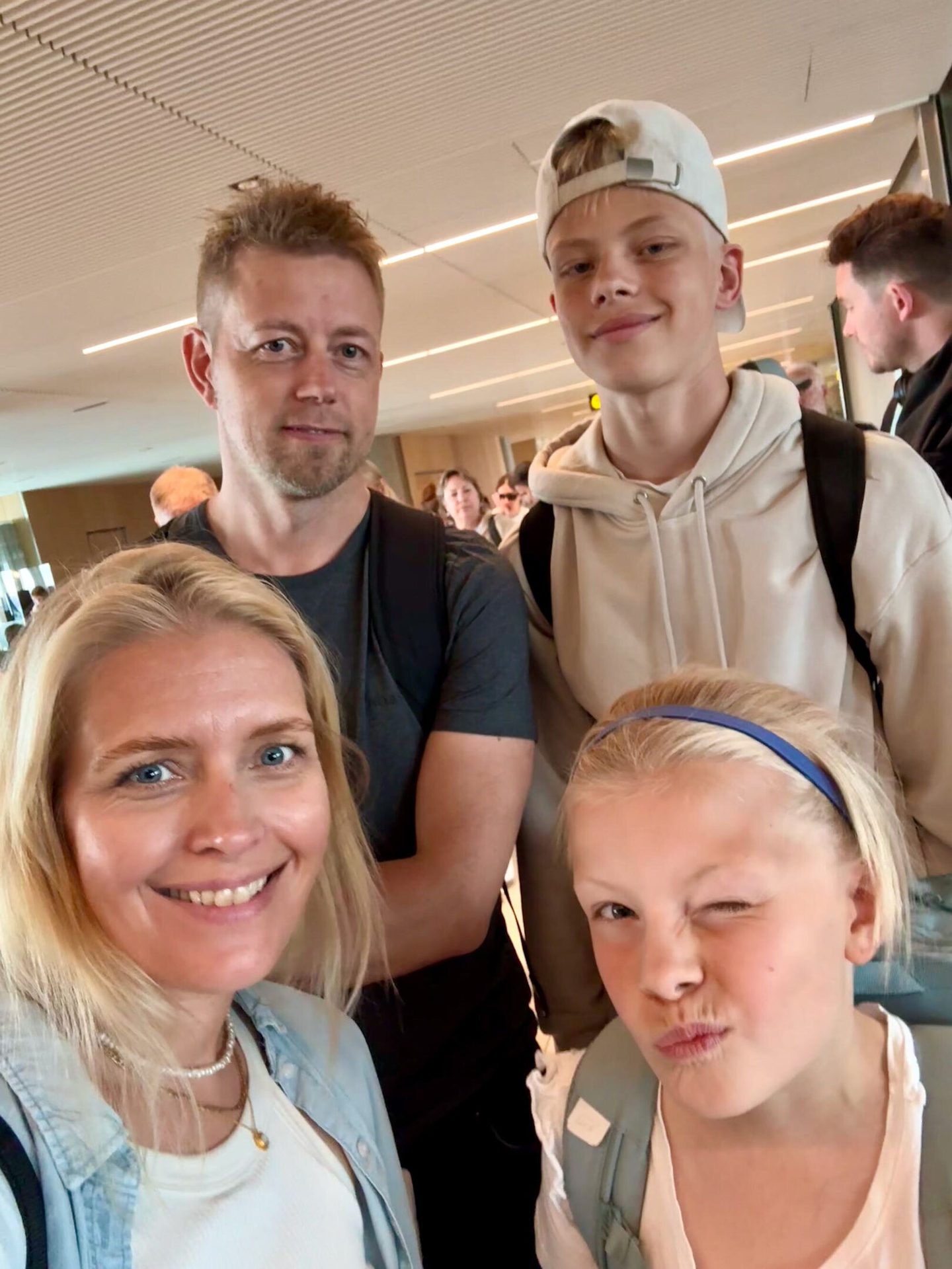 Smiling family of four takes an indoor selfie. The young girl winks.