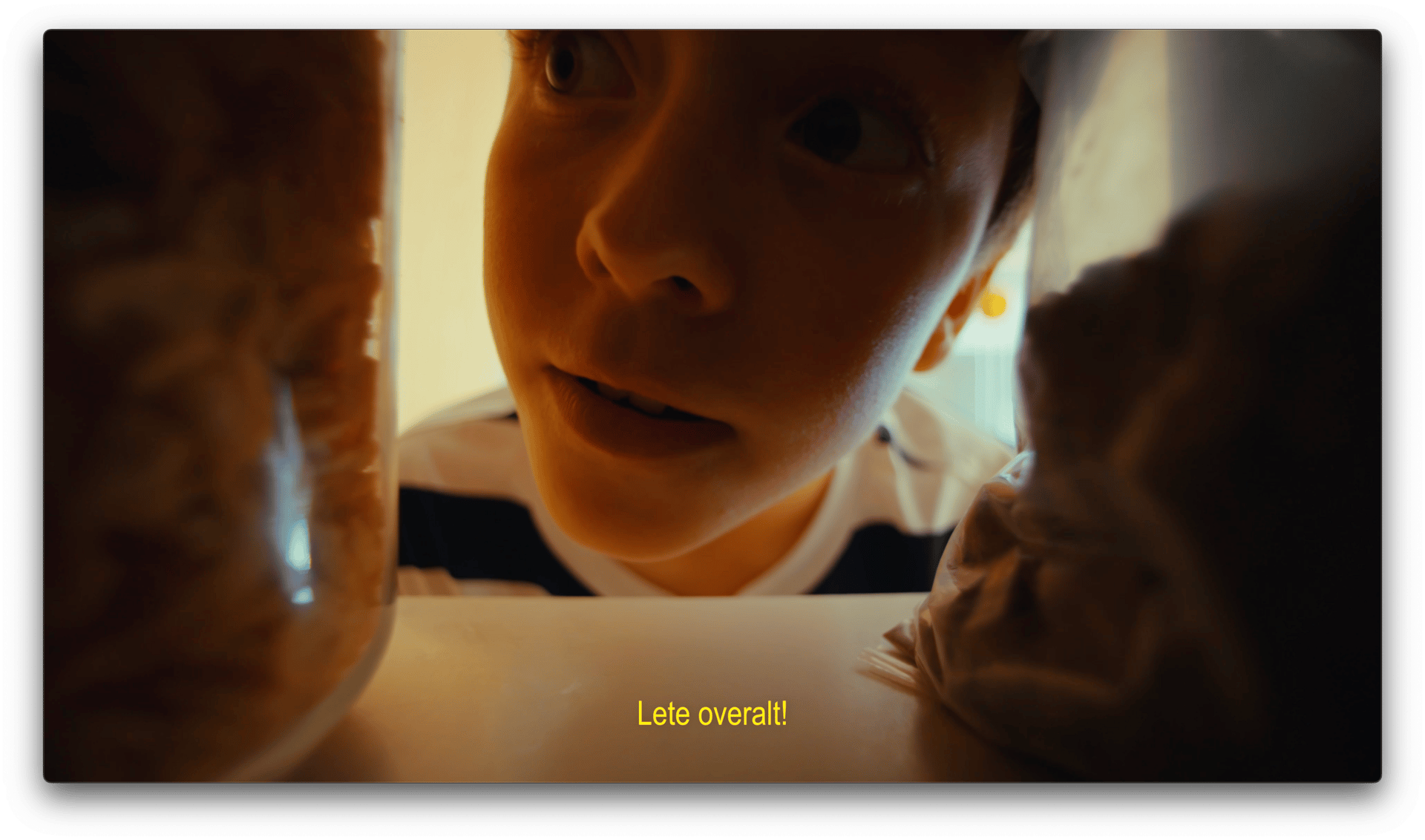 Low-angle view from inside a fridge of a child peering in. Text: "Lete overalt!"