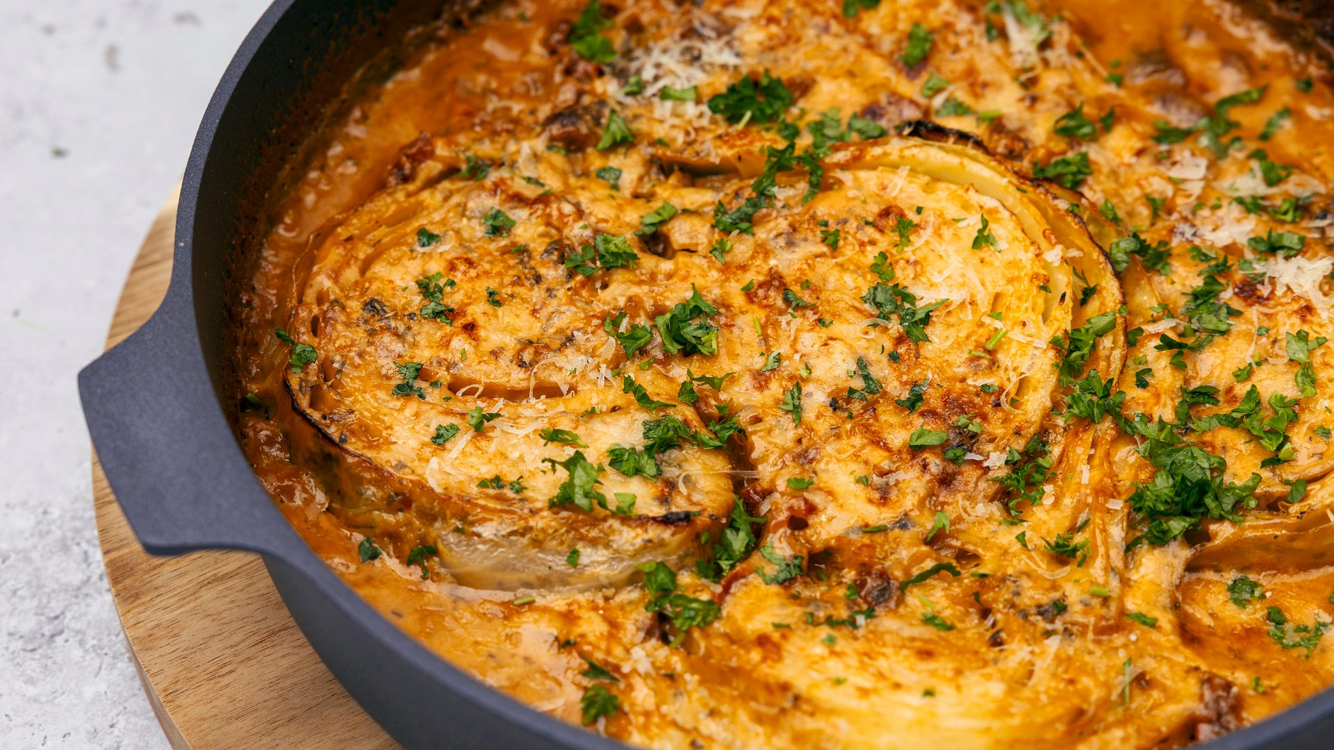 Baked cabbage steaks in a creamy sauce, topped with melted cheese and fresh parsley, served in a skillet.