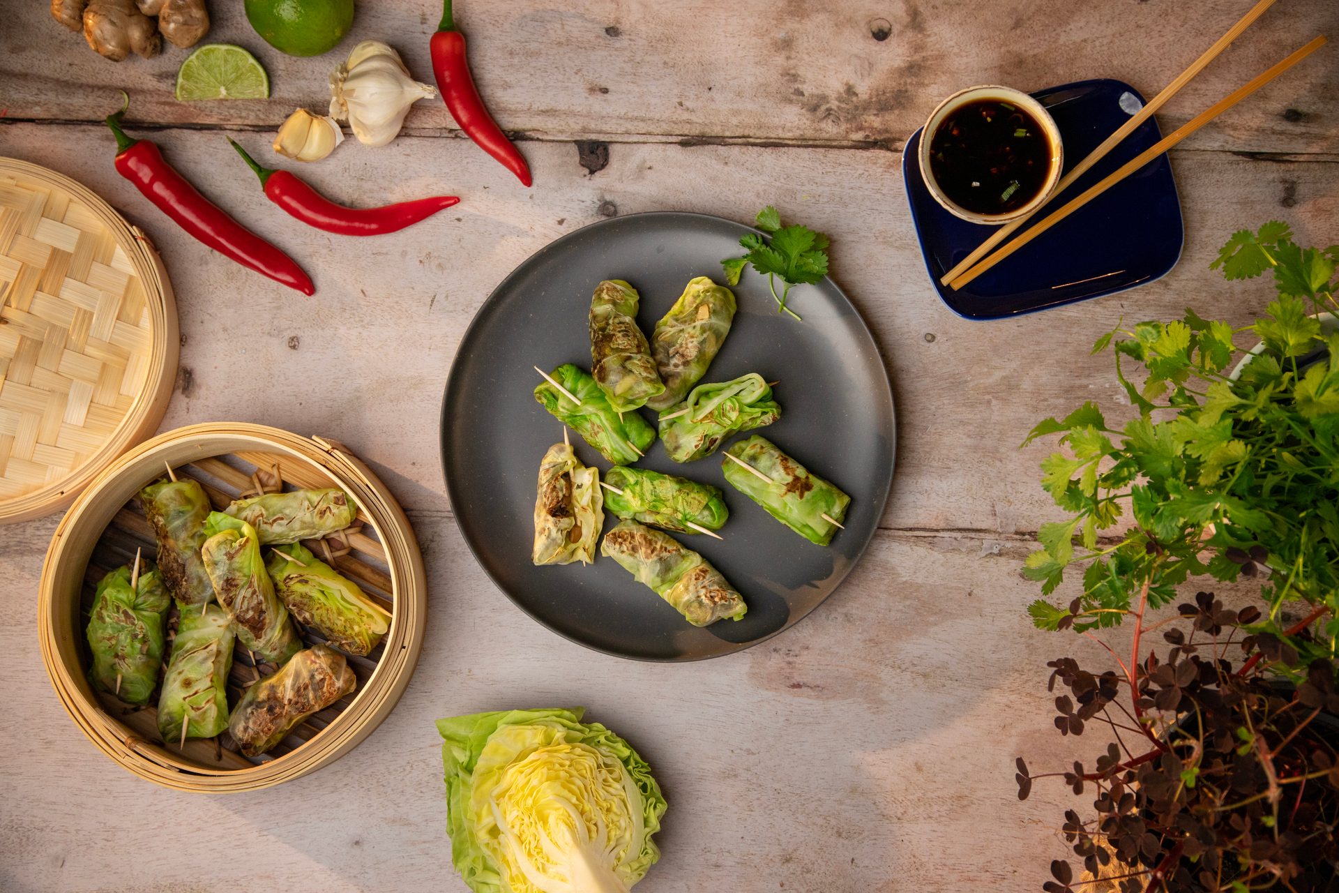 Cabbage rolls with chili, garlic, ginger, lime, cilantro, and dipping sauce on a wooden table.
