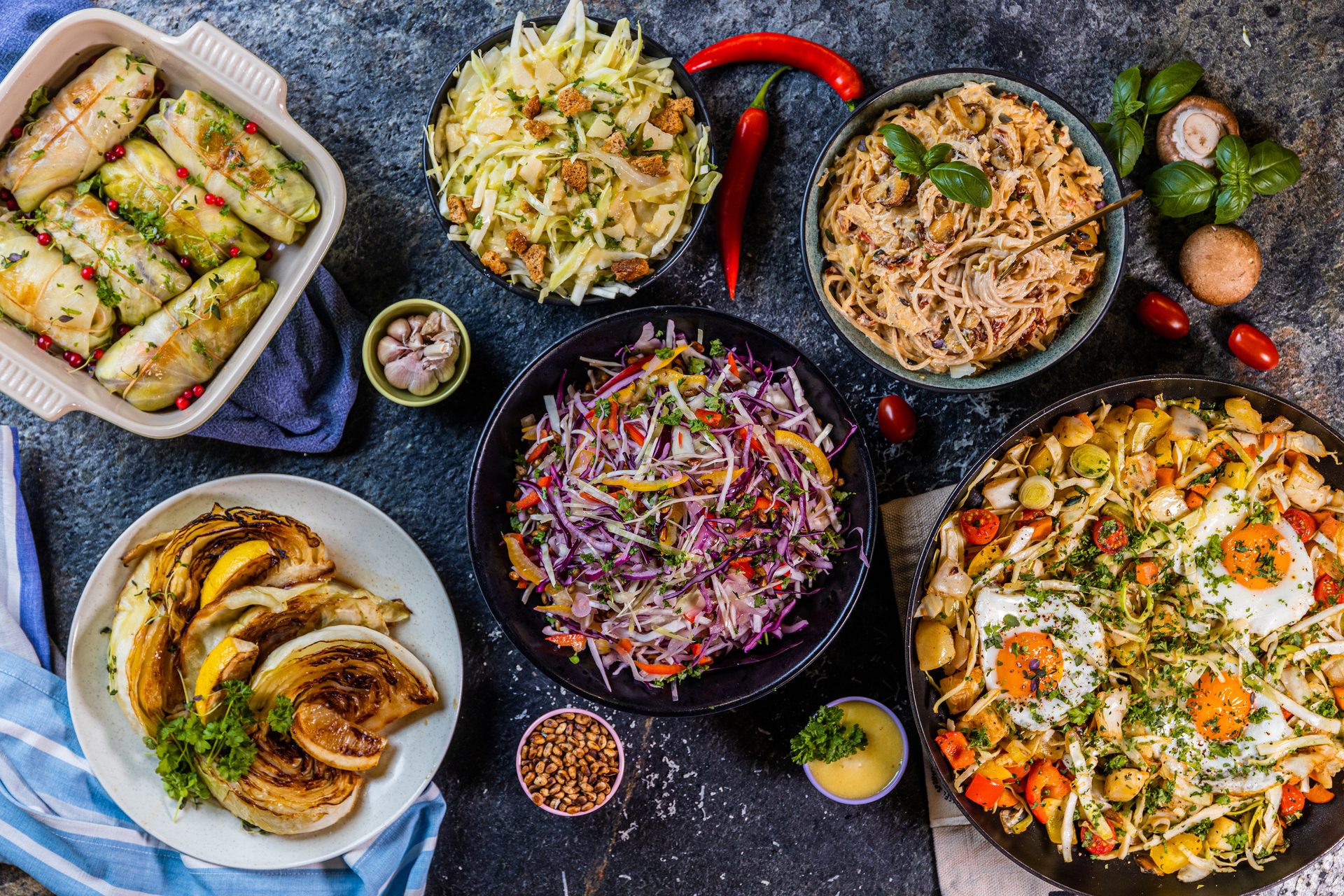 A vibrant spread of dishes: cabbage rolls, salads, pasta, roasted vegetables, and skillet eggs.
