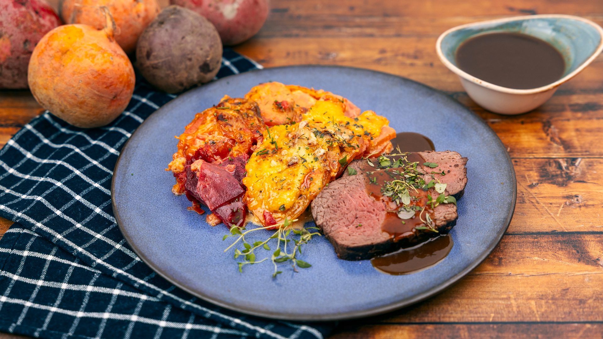 Juicy beef roast, cheesy gratin, and roasted beets on a blue plate, served with gravy.