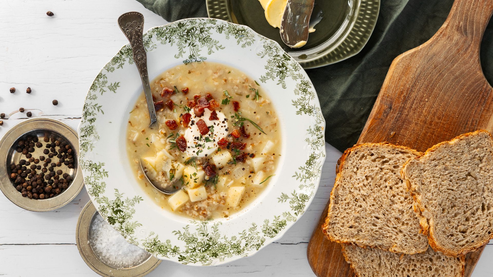 Hearty potato and bacon soup with sour cream and herbs, served with dark bread, peppercorns, and salt.