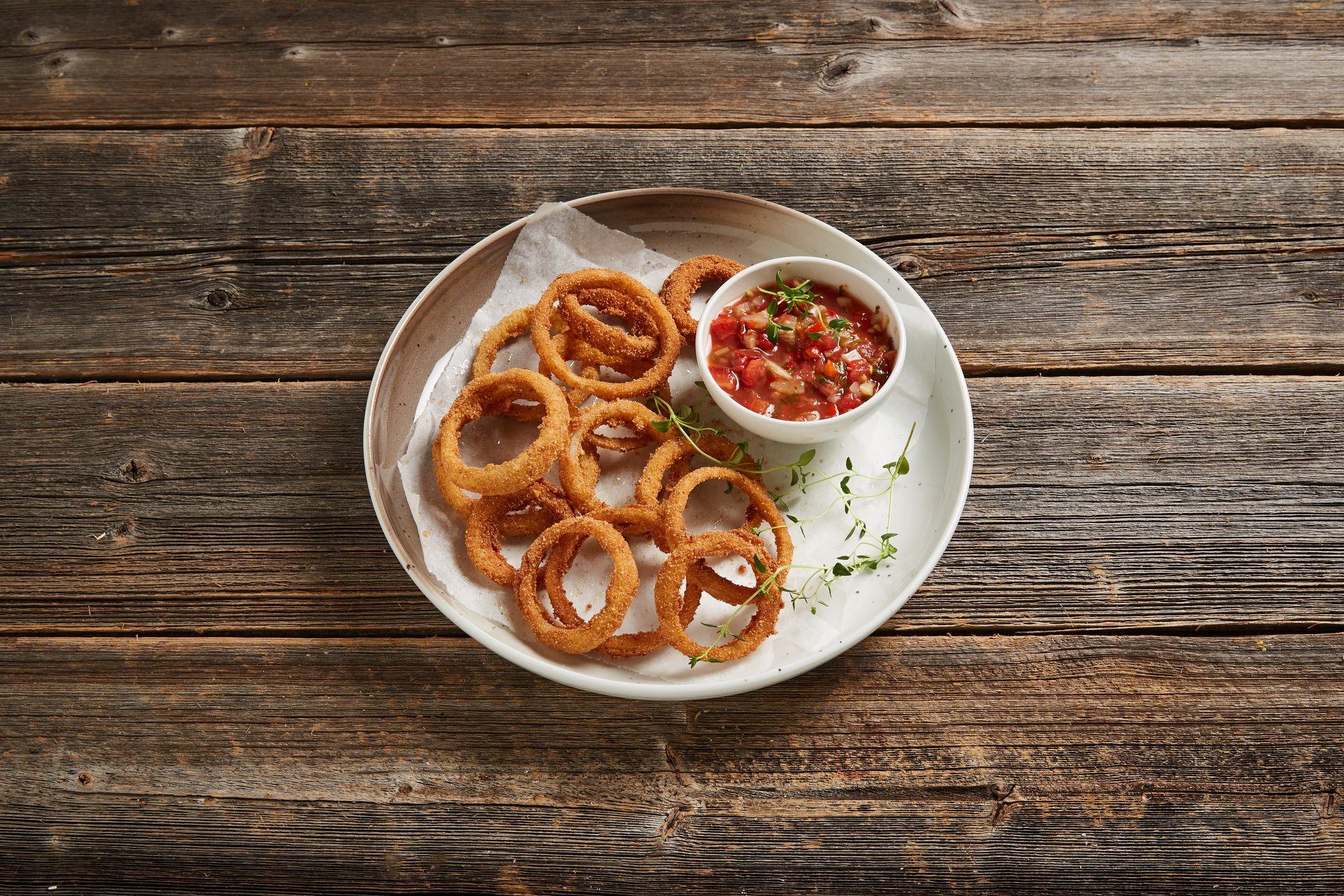 Crispy golden onion rings served on a white plate with a side of fresh tomato salsa on a wooden table.