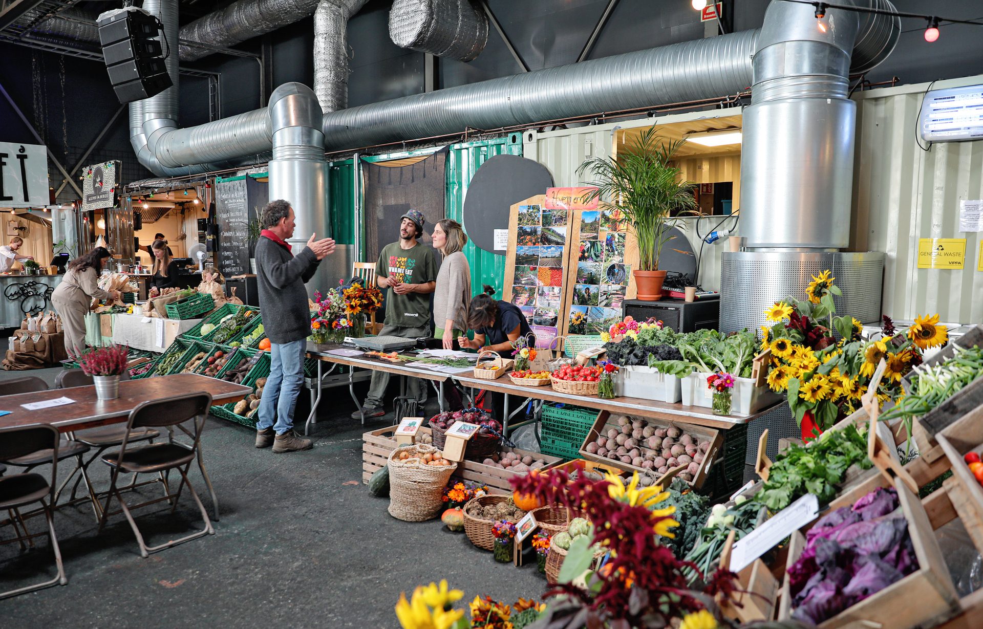 Indoor market with people at a produce stall, fresh vegetables, and industrial architecture.