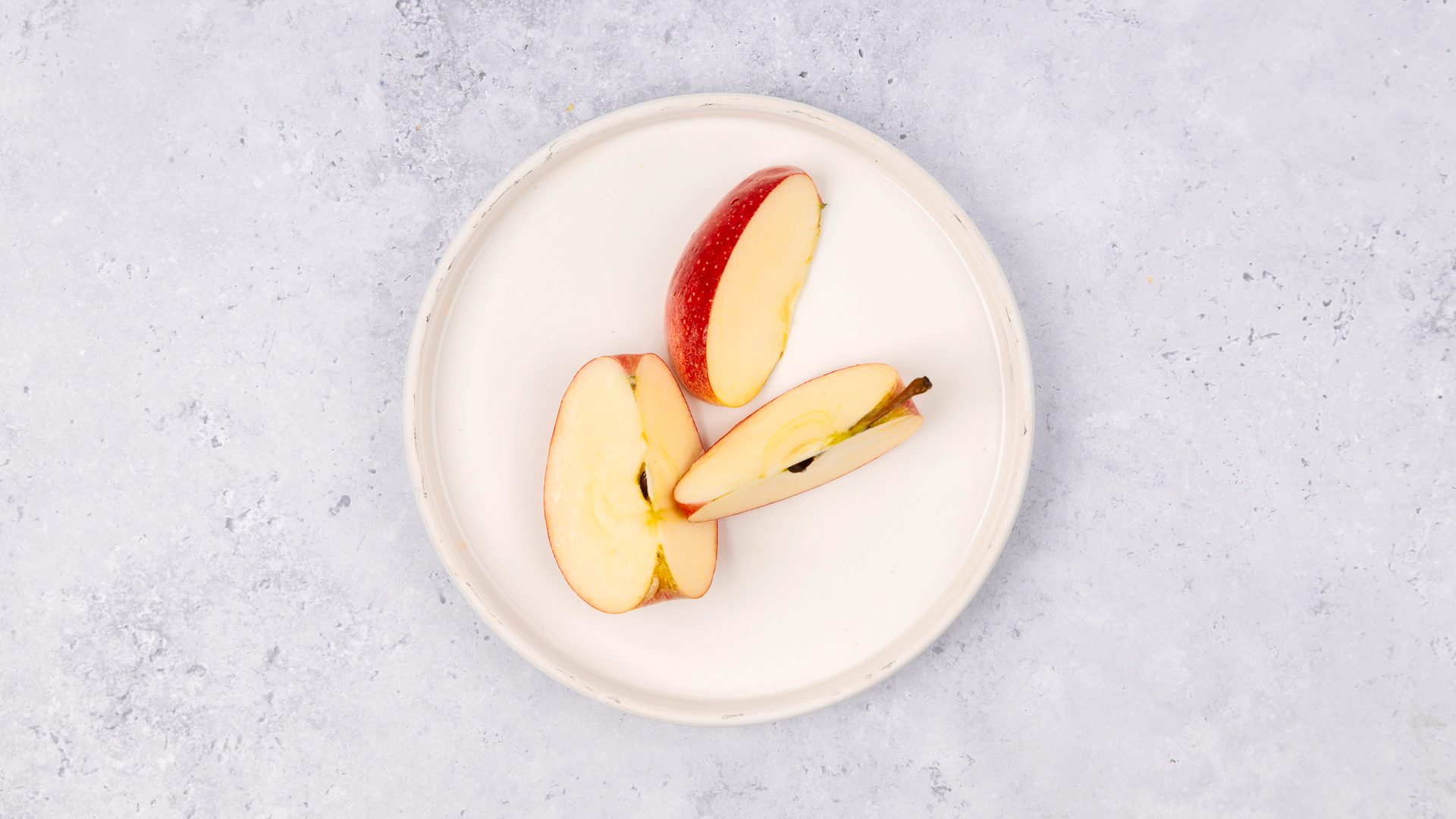 Red apple slices on a white plate with a light grey background.