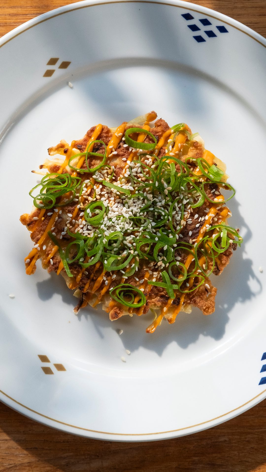 Savory okonomiyaki or similar dish, topped with green onions, sesame seeds, and a creamy sauce on a white plate.