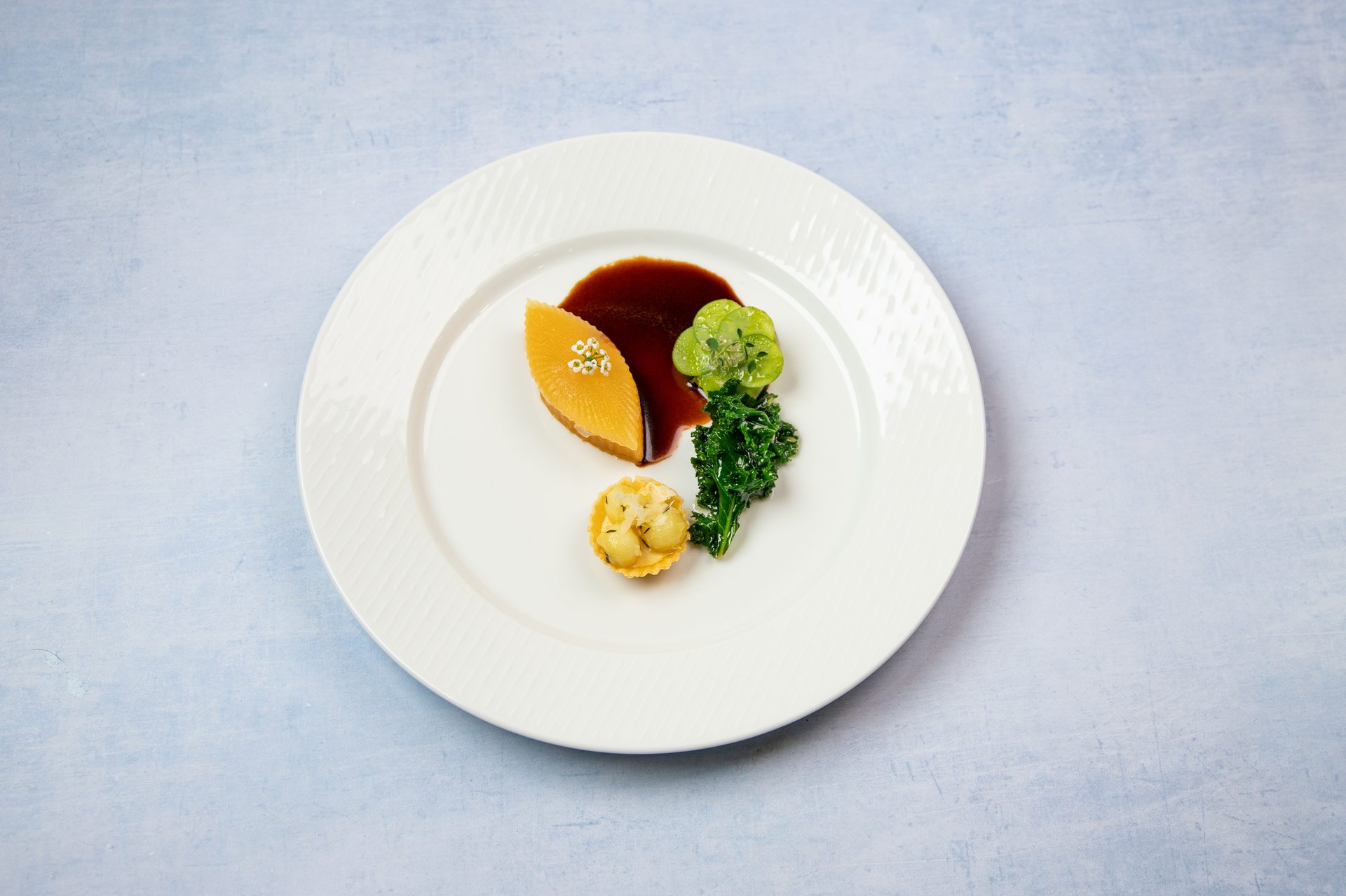 Elegant plated dish with yellow terrine, dark sauce, green vegetables, and a mini tart.