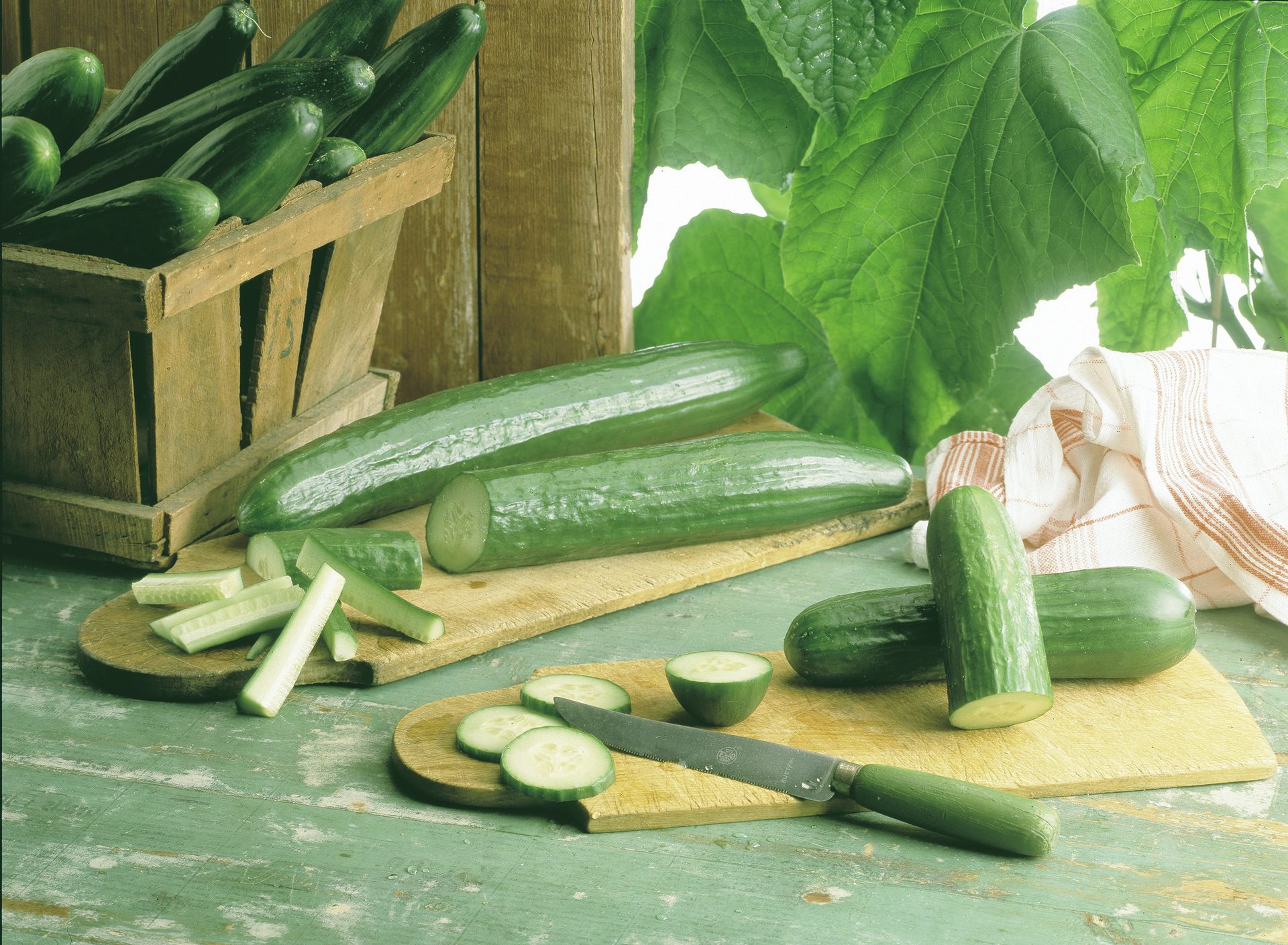Fresh cucumbers, whole and sliced, arranged on cutting boards with a wooden crate and leaves.