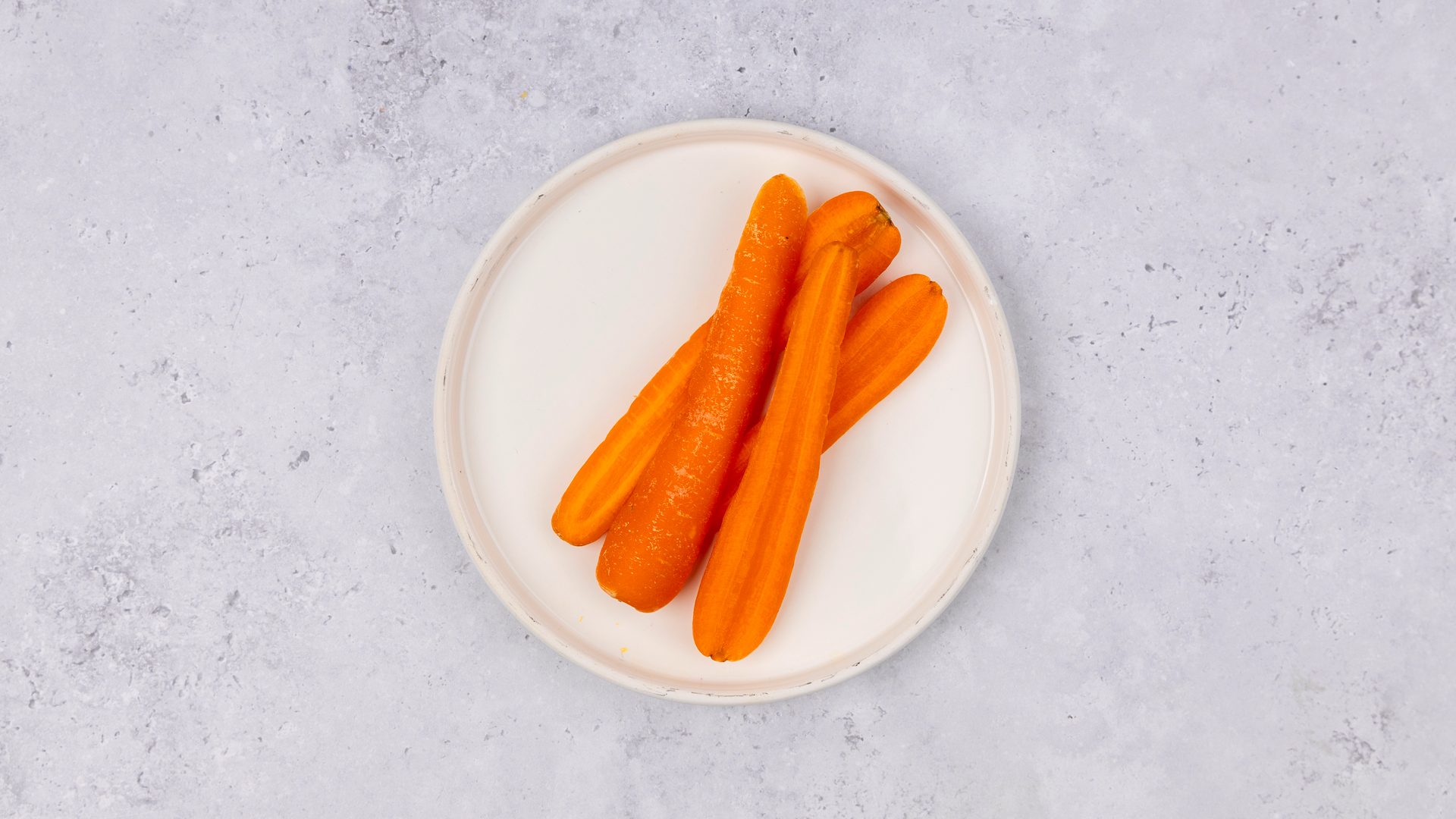 Boiled carrots served on a white plate against a light gray textured background, seen from above.