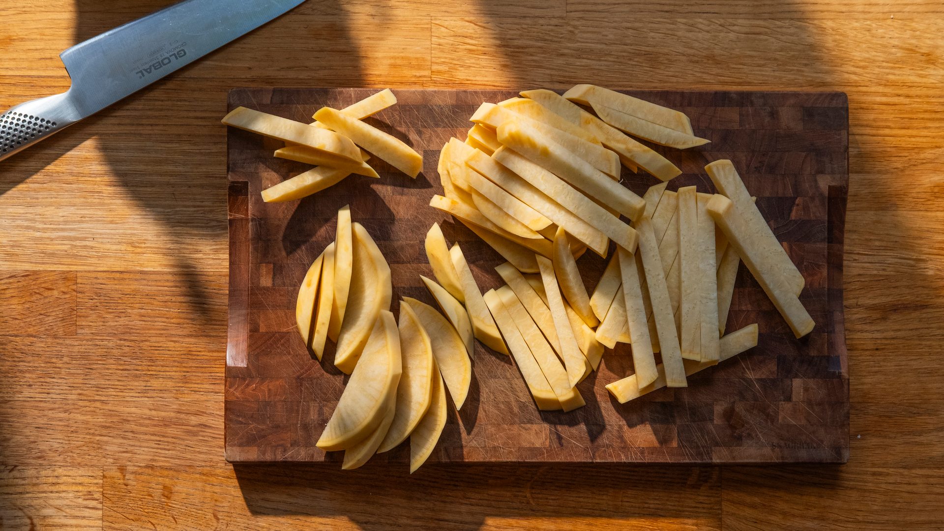Sliced parsnips on a wooden cutting board next to a knife, ready for cooking.