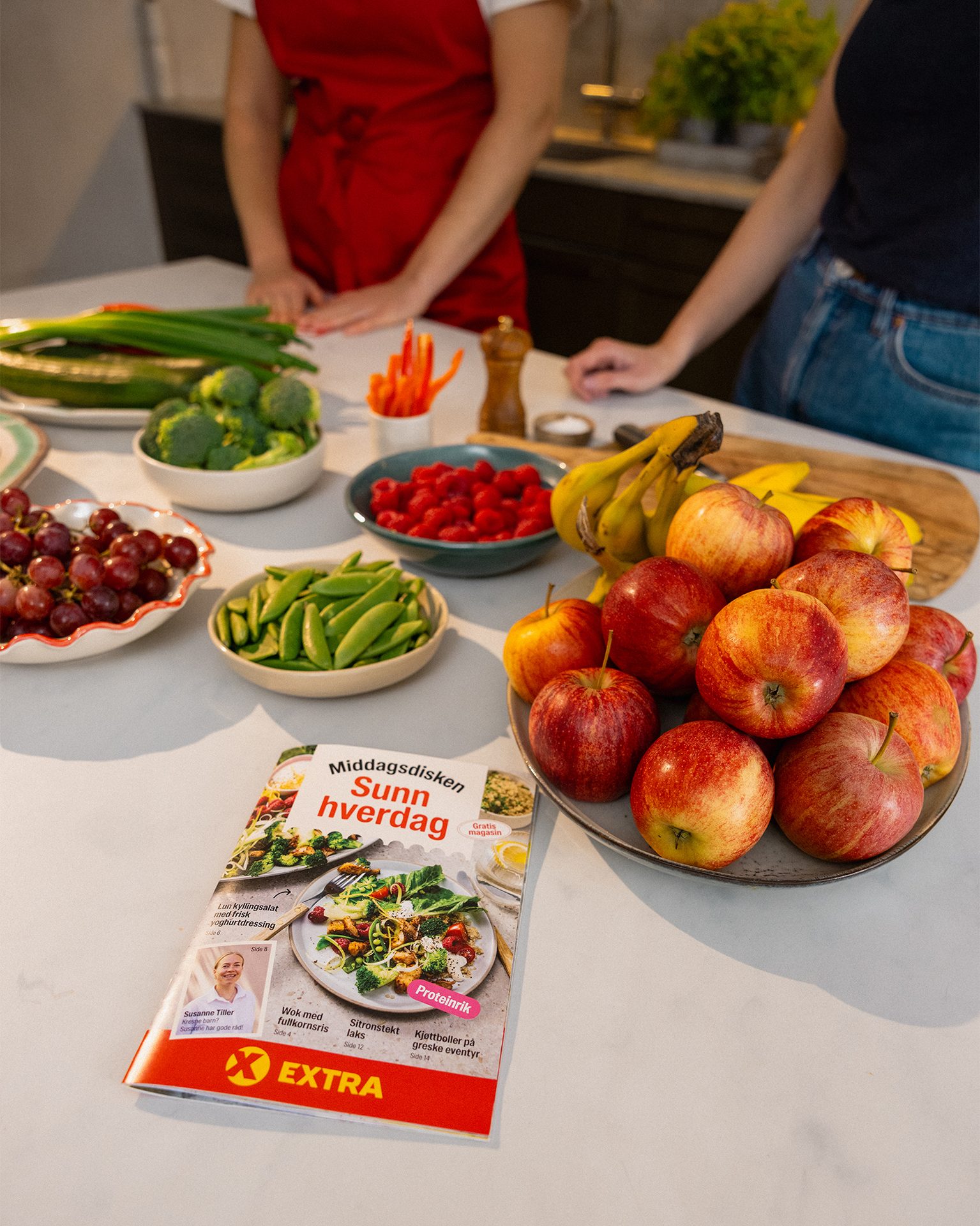 A kitchen counter with fresh fruits and vegetables (apples, berries, broccoli), and a 'Sunn hverdag' recipe magazine.