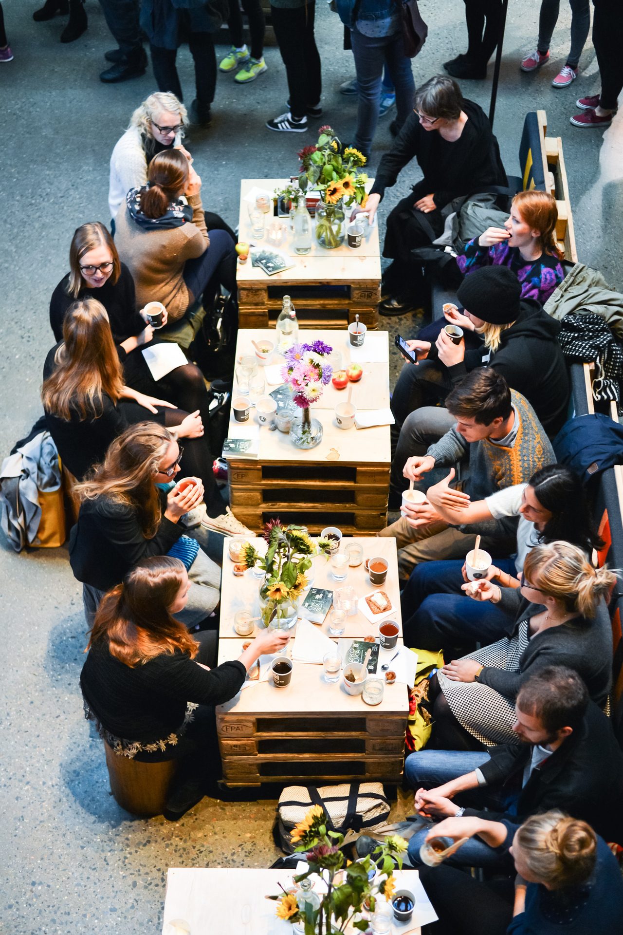 People socialize around pallet tables, enjoying drinks and conversation in an informal setting.