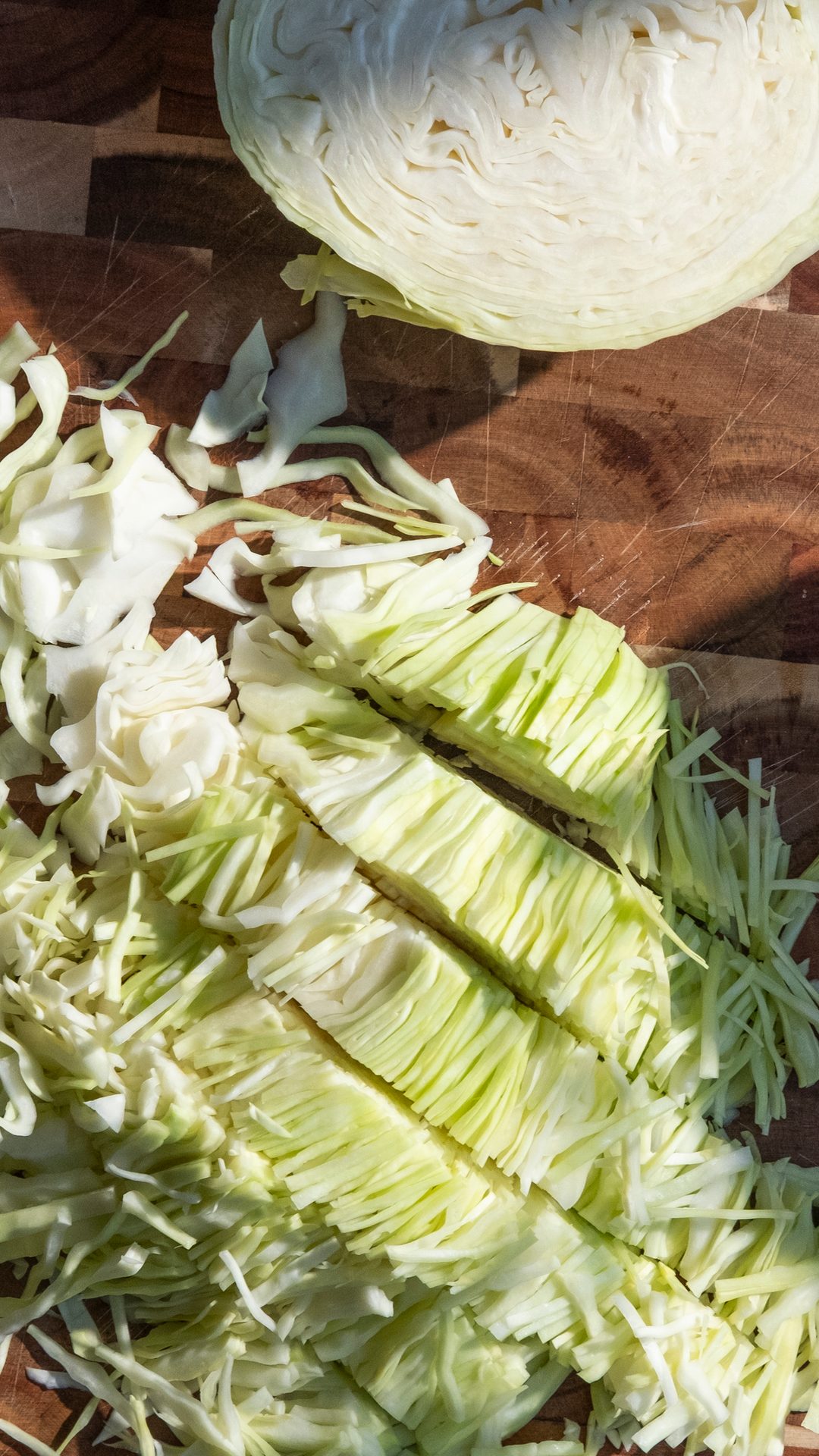A head of green cabbage, partially cut, with shredded and sliced pieces on a wooden cutting board.