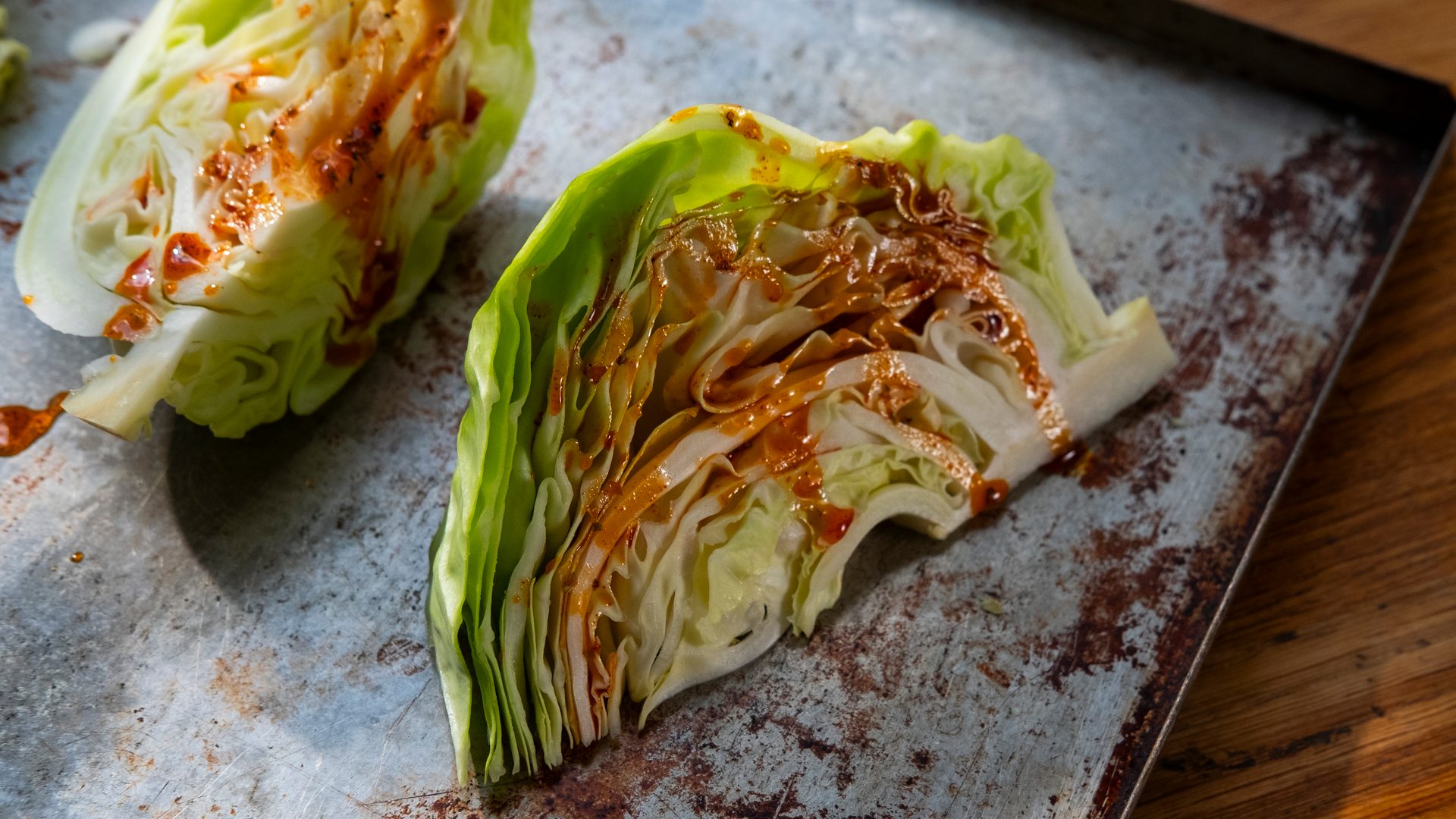 Two halves of iceberg lettuce, drizzled with sauce, on a rustic baking sheet, ready for roasting.